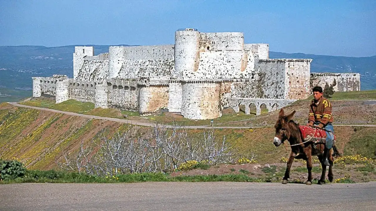 Junge reitet auf einem Esel vor der imposanten Festung Krak des Chevaliers, einst ein wichtiger Stützpunkt der Johanniter-Kreuzritter.