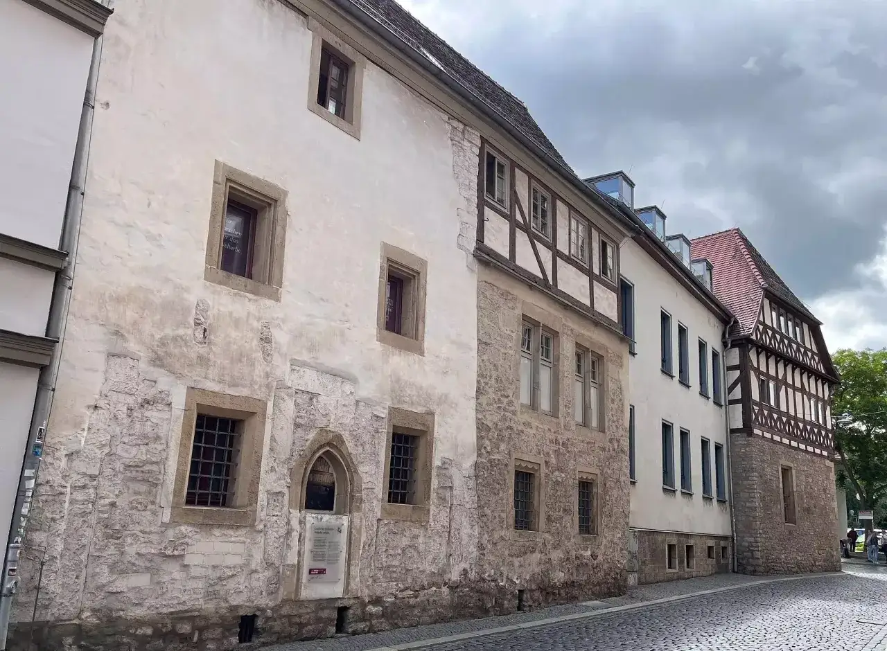 Alte Fachwerkhäuser und Steingebäude säumen eine Kopfsteinpflasterstraße. Ein Schild deutet auf die Geschichte der Juden im Mittelalter hin.