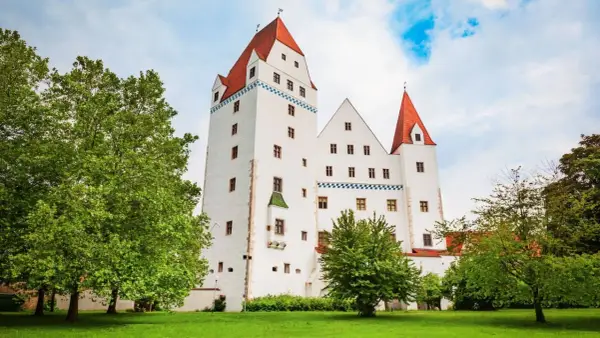 Das weiße Schloss Ingolstadt mit roten Dächern und grünen Bäumen im Vordergrund.