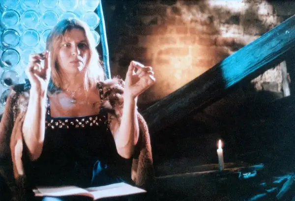 Annamirl Bierbichler in dunklem Kleid mit Pelzmantel, die Hände erhoben, im Schein einer Kerze.
