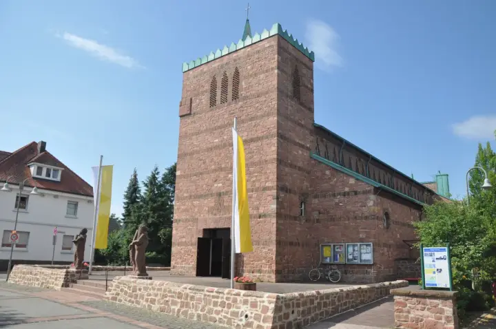 Kirche in Dettingen am Main mit roten Ziegeln, Fahnen und Statuen vor dem Eingang.