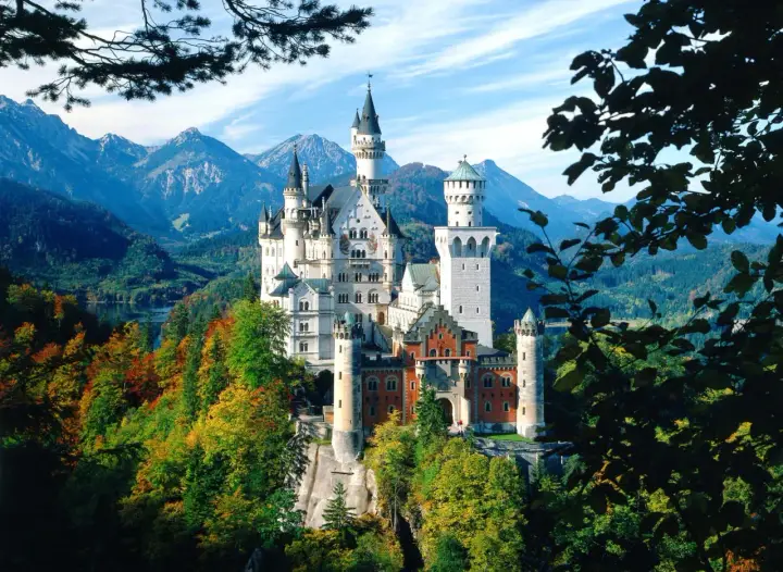 Märchenhaftes Schloss Neuschwanstein thront auf einem Felsen, umgeben von bunten Herbstwäldern und majestätischen Bergen.