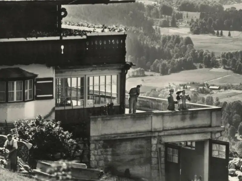 Blick auf die Hitler-Residenz mit Personen auf dem Balkon und einer malerischen Landschaft im Hintergrund.